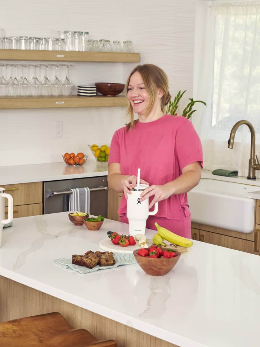 A woman making infused water in Hydro Flask Travel Tumblers, laughing in the kitchen.