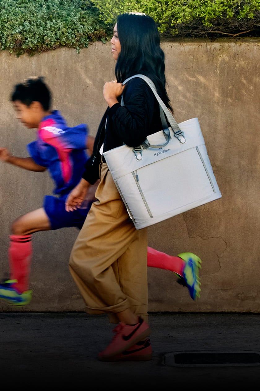 Mom with son in soccer uniform strolling down a sidewalk carrying a hydro flask carryout tote